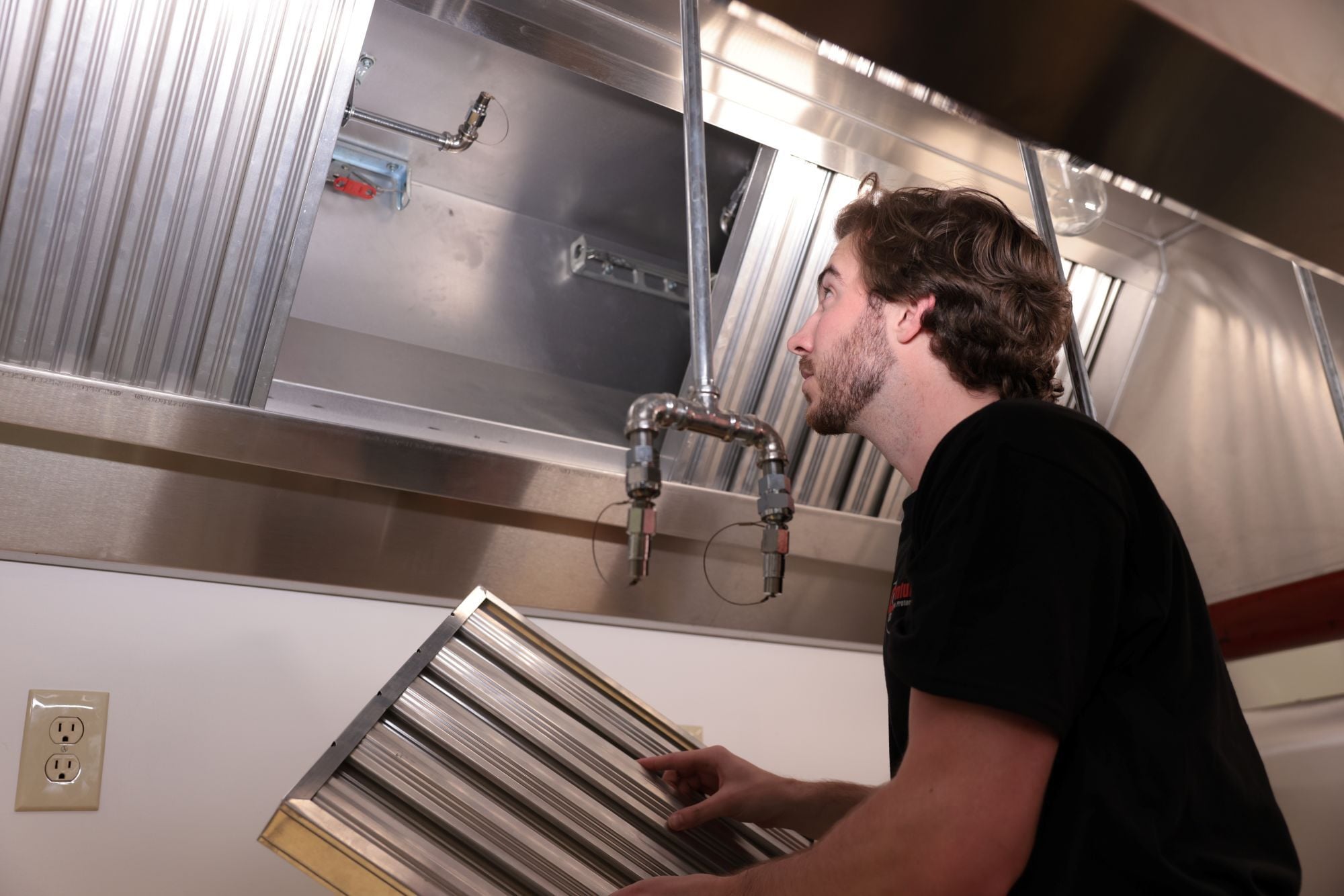 Technician inspecting a commercial kitchen hood fire suppression system
